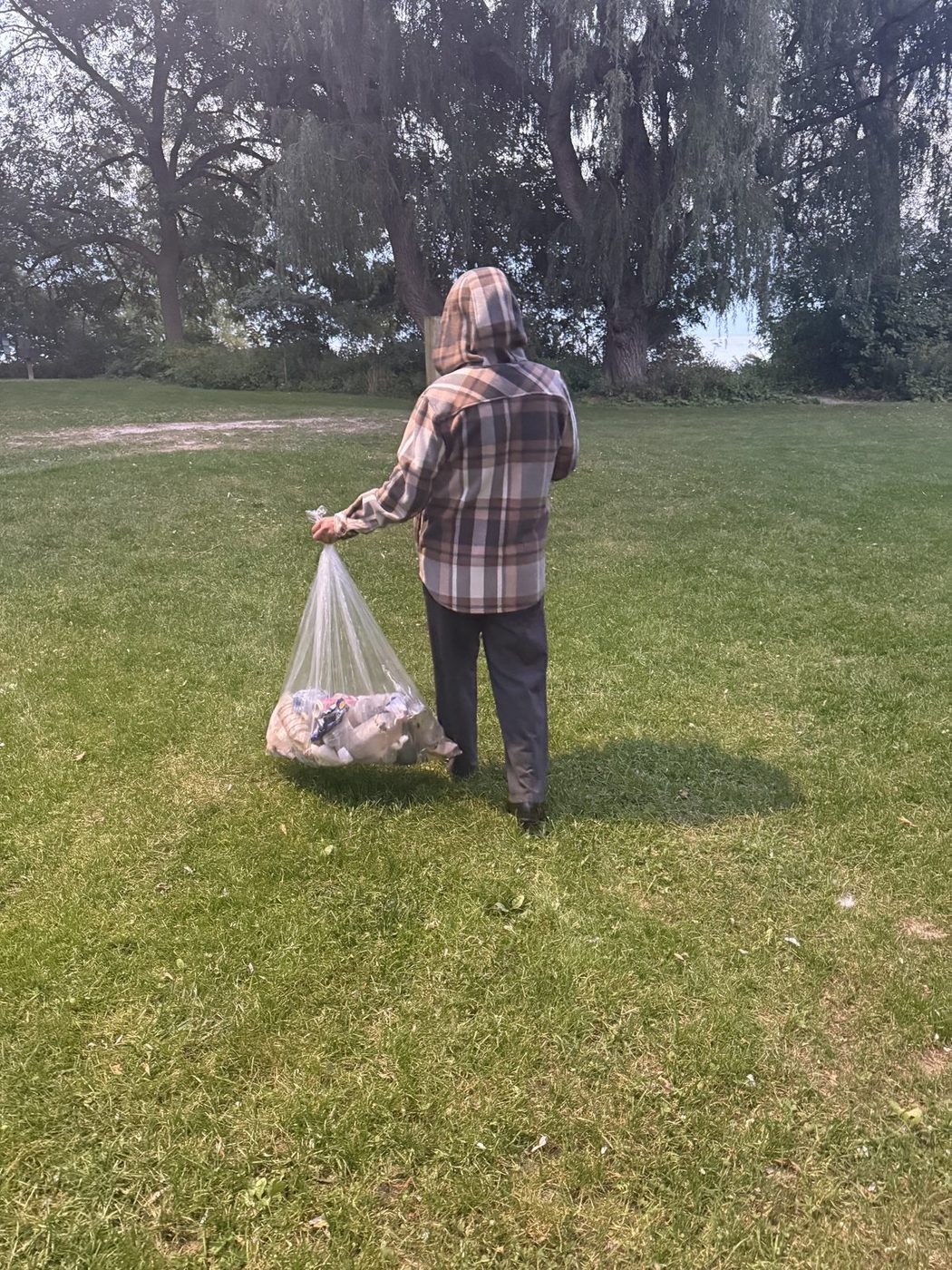 A volunteer carrying a bag of collected litter at a park cleanup