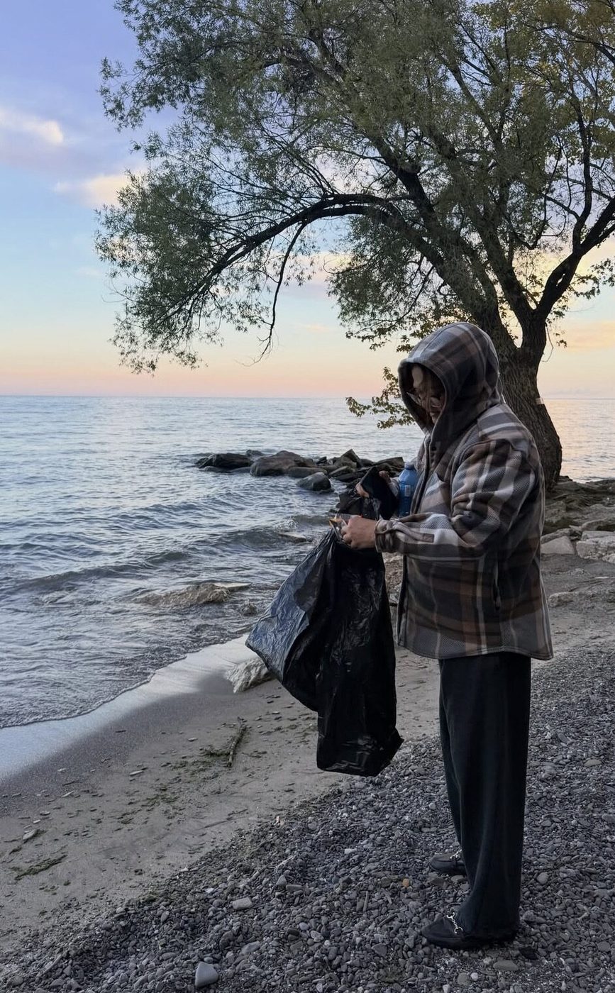 A MiVolunteer volunteer collecting litter along the lakeshore at sunset