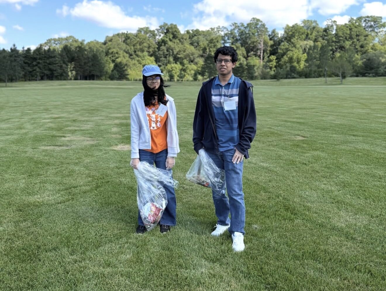 Two MiVolunteer volunteers with collection bags at a sunny park cleanup